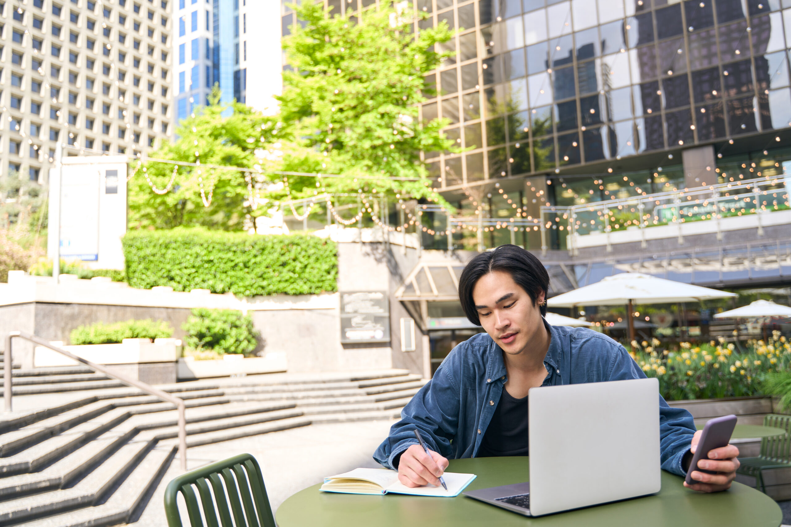 Asian writer man using laptop computer taking notes, working project outdoors. Pensive handsome Japanese author creating book at greenery place copy space